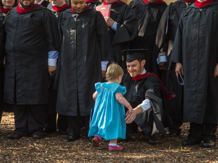 一位毕业生跪下来拥抱他年幼的女儿.